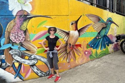 Mrs. ItchyFeet in front of hummingbird mural in Comuna 13